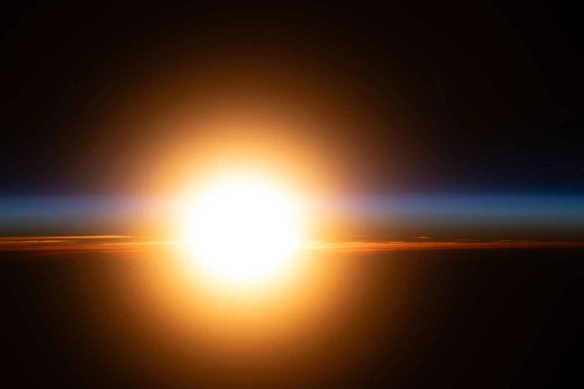 A bright orange sunburst illuminates Earth’s atmosphere during an orbital sunrise
