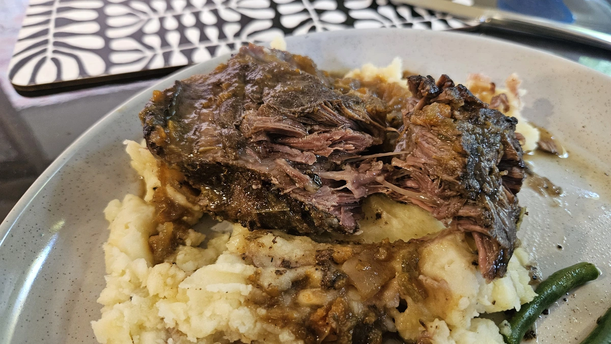 cooked beef cheek pulled apart over mashed potatoes on a plate. Stray green bean on the side. 
