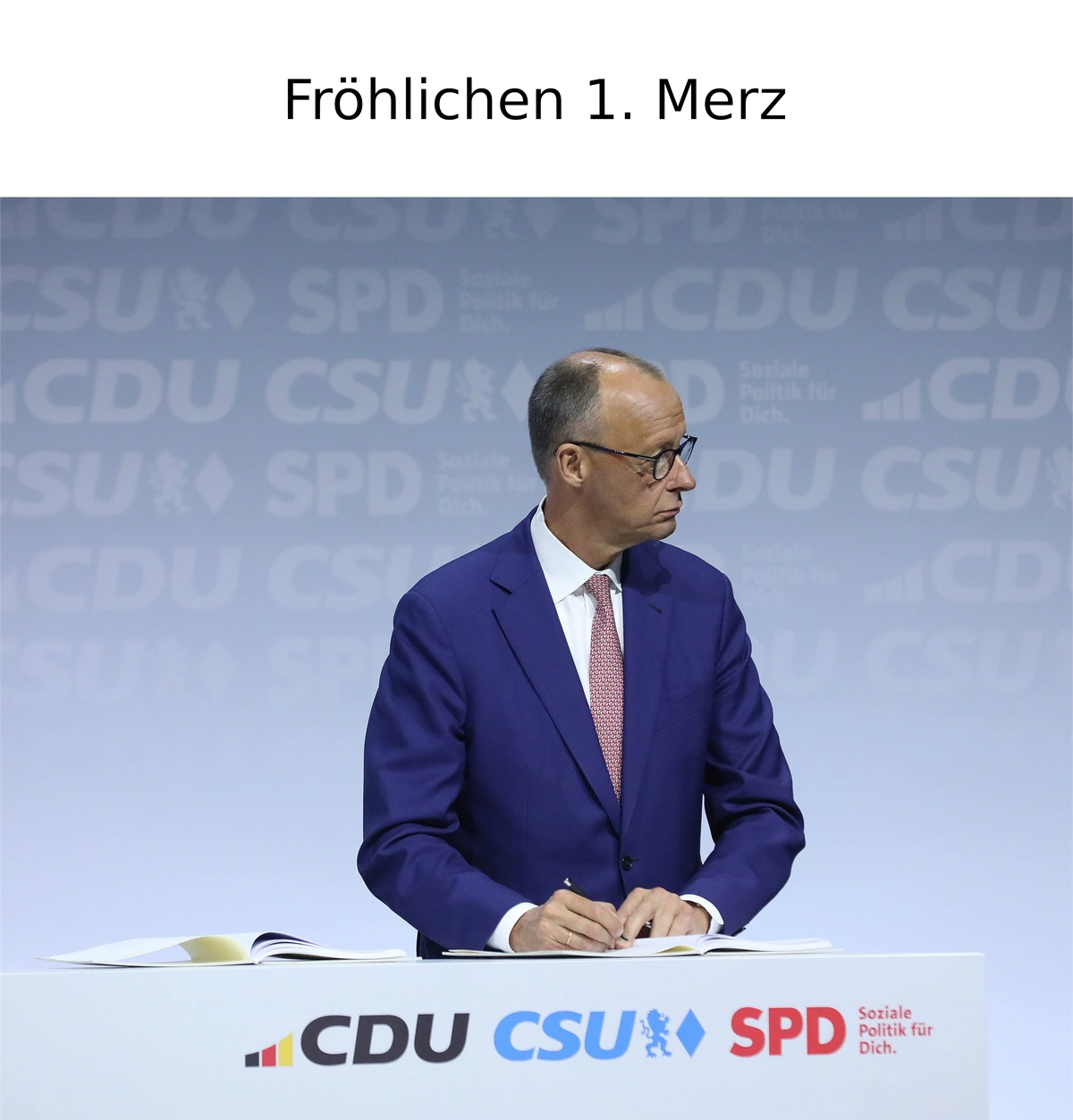 Friedrich Merz schaut auf der Bühne weit nach rechts. Darüber steht 'Fröhlichen ersten Merz'