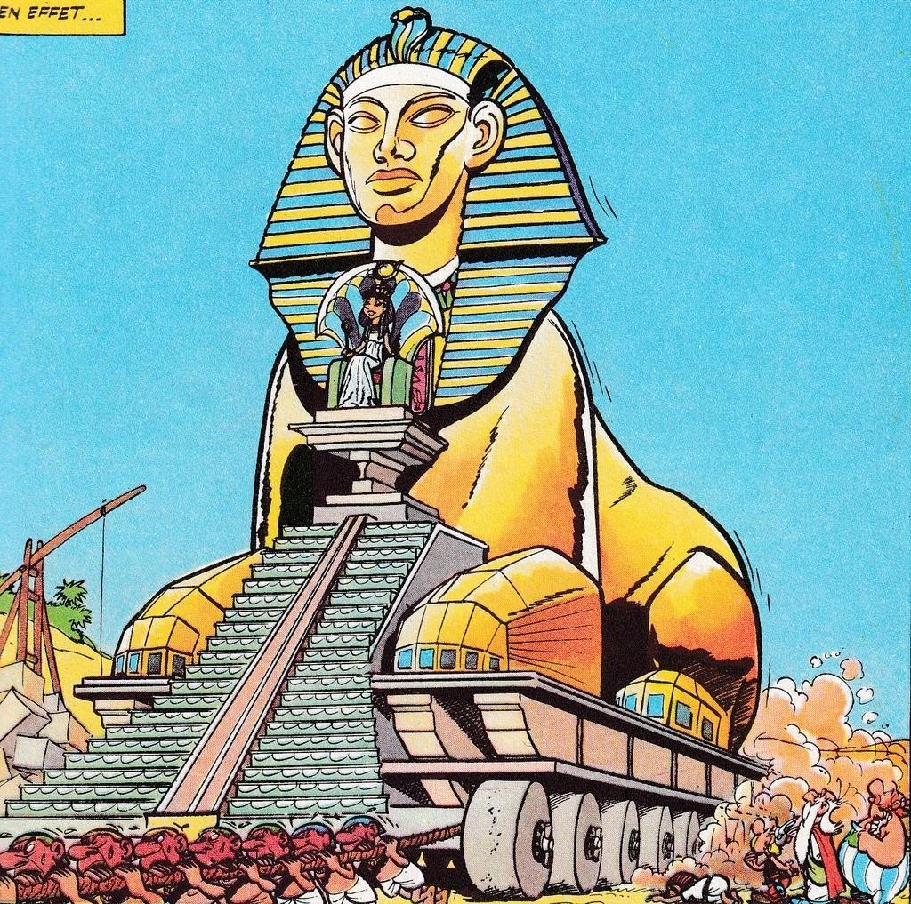 a cartoon pic of Cleopatra being hauled in a huge Sphinx-chariot pulled by humans, while Asterix Obelix Getafix watch, and an Egyptian person prostrates himself