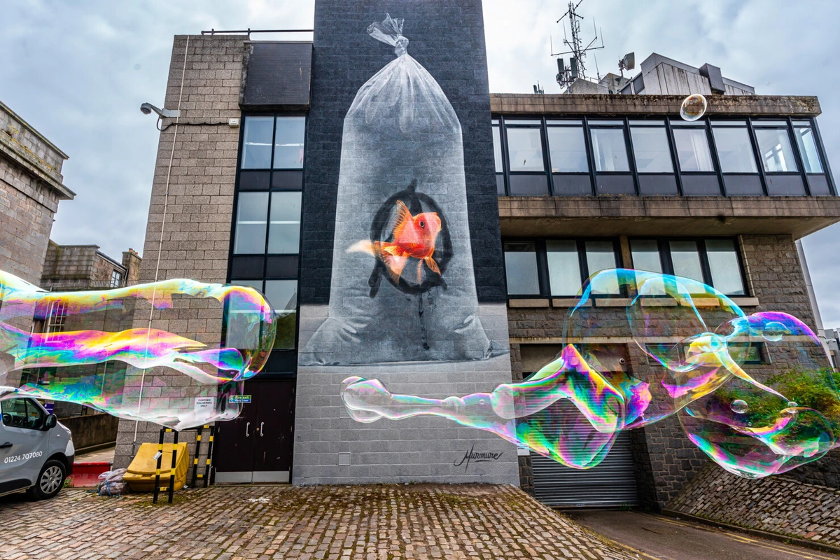 A large mural of a goldfish inside a plastic bag of water, with the anarchist A drawn on the inside of the bag as if by the fish