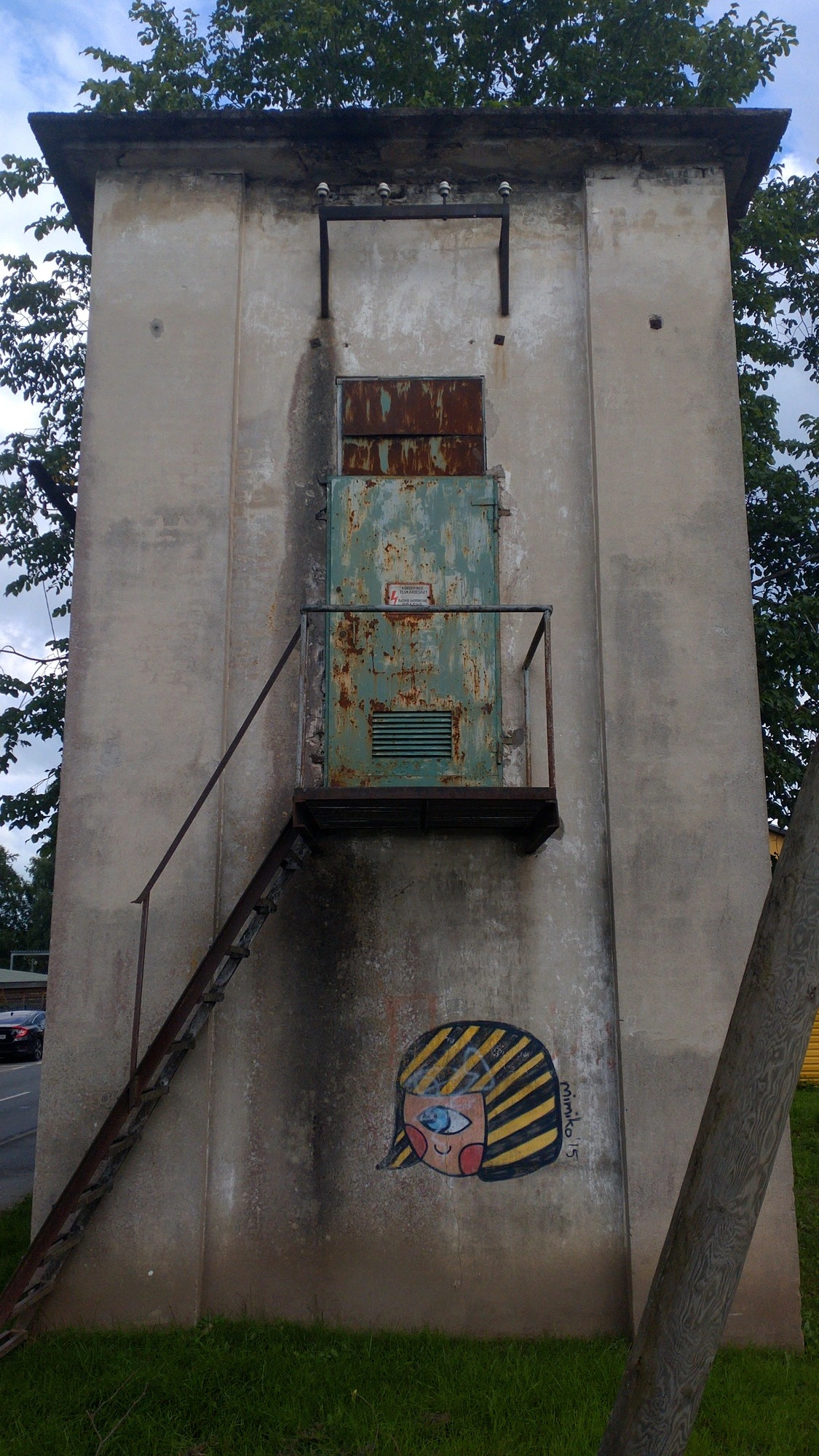 electro tower with rusty door and graffiti of a one-eyed girl's head with black/yellow striped hair