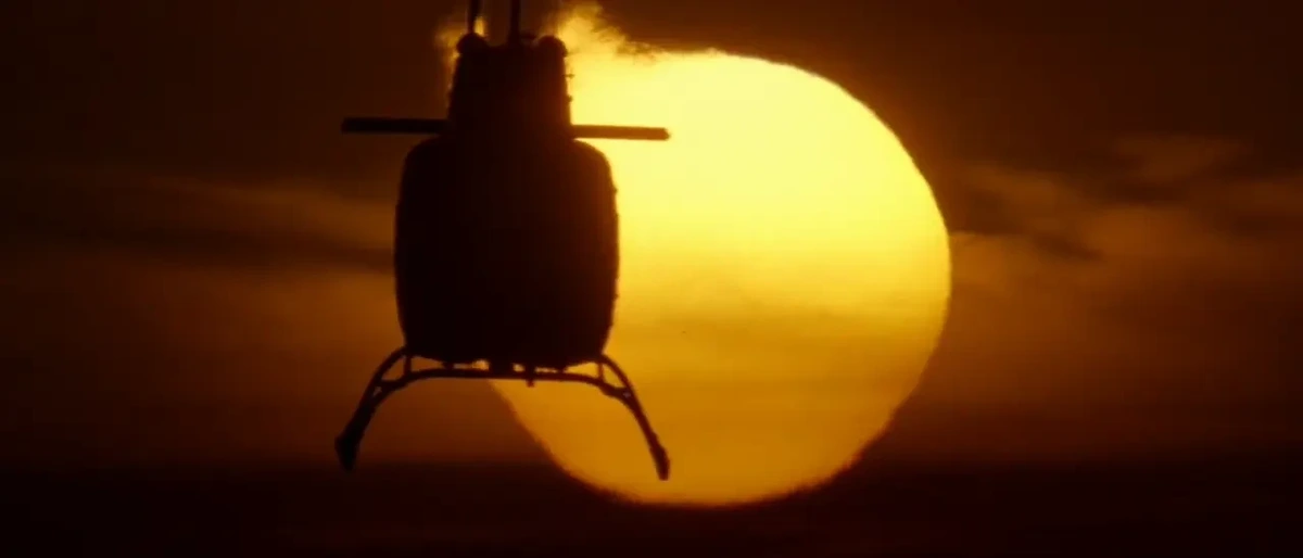 A helicopter in flight silhouetted against an orange sun at sunset/sunrise