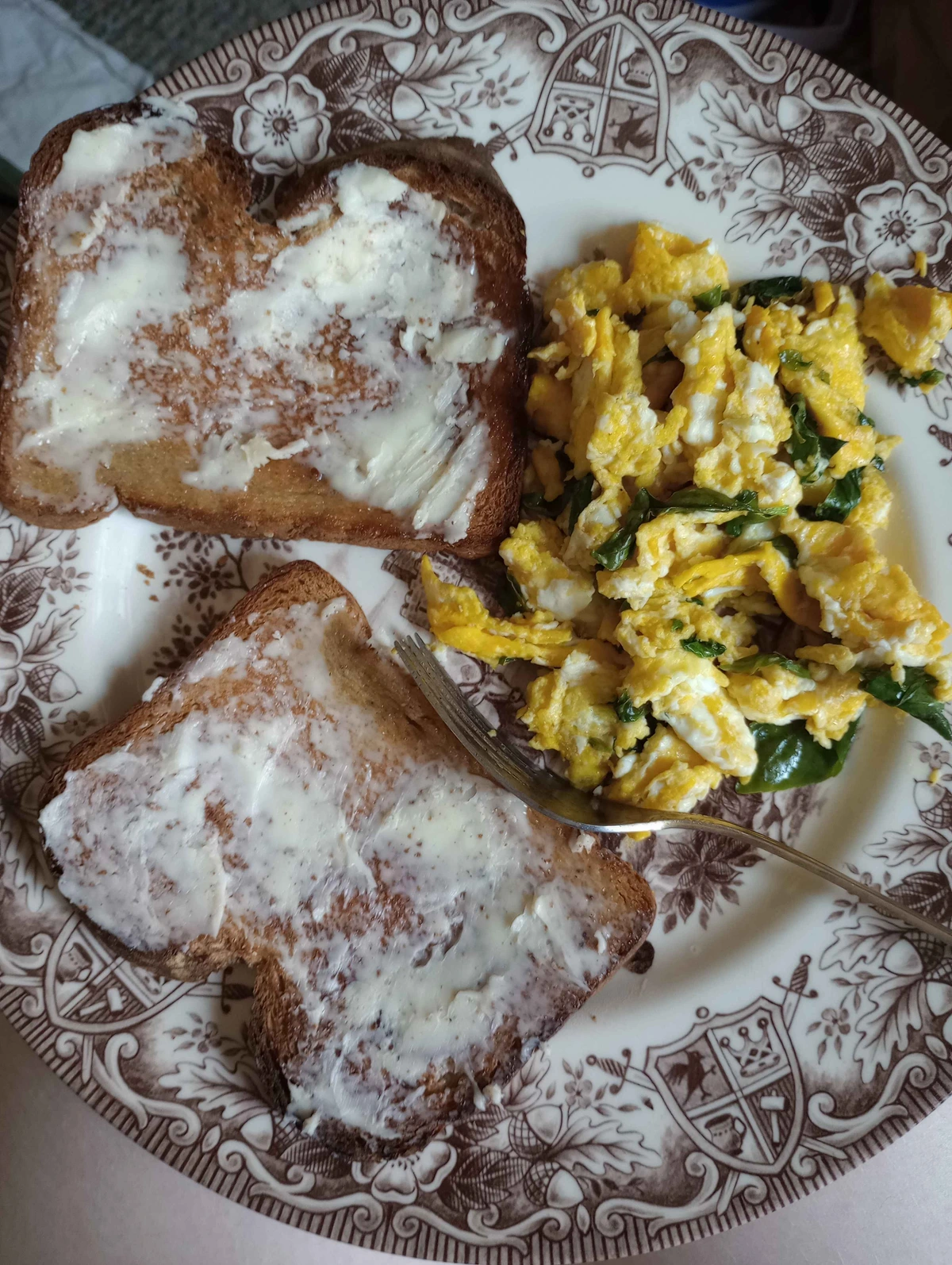 A plate with two slices of buttered toast and some scrambled eggs with basil mixed in