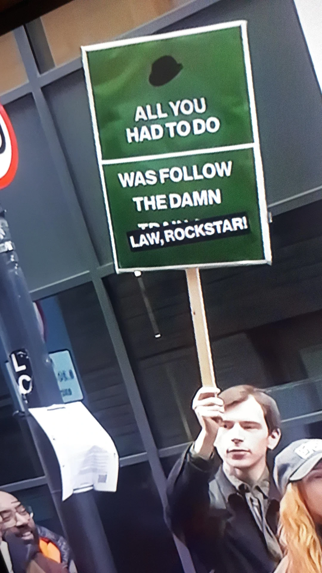 Man striking in front of Rockstar office holds a banner saying "all you had to do was follow the damn law, Rockstar"