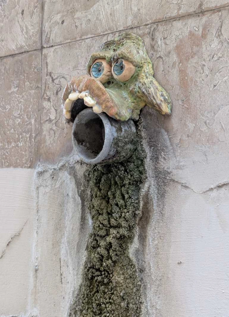 ceramic that looks.like.the fave of a goblin or another fantasy creature. the face is placed above a waterpile which makes tge pipe look like part of the mouth