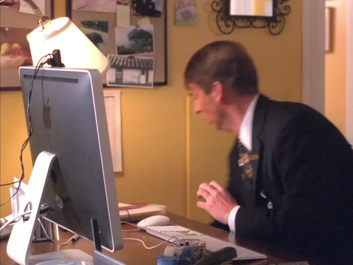 Kenneth looks at a computer screen with a frightened expression, then unplugs it
