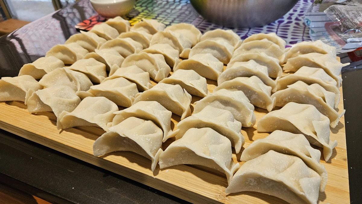 Five rows of six hand made pork dumplings on a wooden cutting board. 